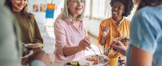 Older adult paints with friends in a sunny studio, showing independence and social connection at Farmington Square Beaverton.