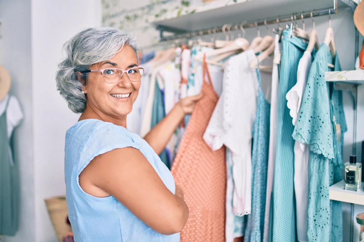 Resident Independence, Farmington Square Beaverton Smiling older woman chooses an outfit from a tidy closet, showing resident independence at Farmington Square Beaverton.