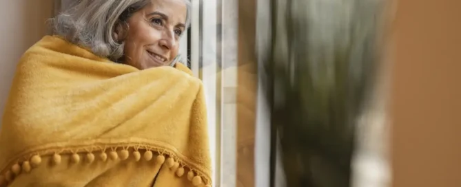 Older woman by a window on a winter day, showing signs of Seasonal Affective Disorder