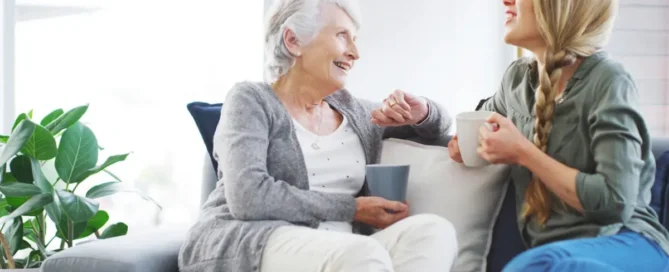 Senior mother and adult daughter talking on sofa about stages of dementia care options