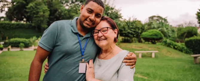 A volunteer sits with an elderly man in a nursing home setting, offering compassionate support, representing the personalized care and human connection that matter most for people living with different types of dementia.